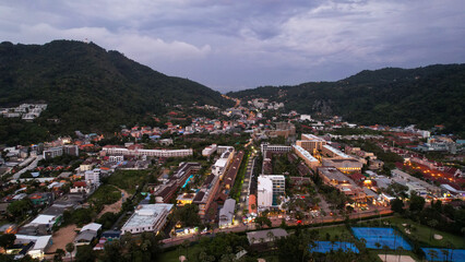 Aerial view of the island at sunset from a drone. Tall palm trees and trees grow. In the distance there are hotels, sports fields, green hills and pink clouds. A place to rest. Phuket Island, Kata