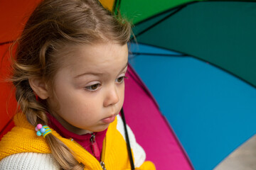 A 3-year-old girl hides in the rain under a colored umbrella