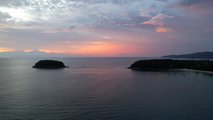 The red-orange sunset is reflected with clouds in the sea. An island can be seen in the distance. Smooth water is like a mirror. There is a lonely island. Not far from the shore of the boat. Epic