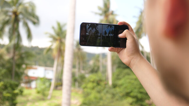 Young man with mobile phone taking photo in a jungle. Close up view of hands on blurred nature background.