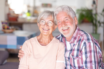 Attractive joyful and smiling senior couple hugging at home looking at camera. Strong relationship for two Caucasian seniors having fun together