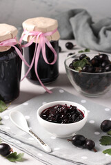 Homemade yoshta jam with whole berries, in a bowl and glass jars on light gray background