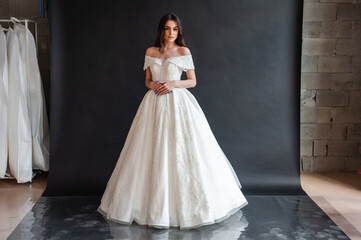 Fototapeta premium Beautiful young sexy model female bride with dark hair in gorgeous glossy long light wedding dress posing in dark studio