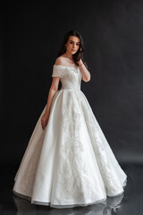 Beautiful young sexy model female bride with dark hair in gorgeous glossy long light wedding dress posing in dark studio