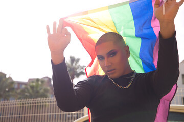 Portrait of non-binary person, young and South American, heavily make up and holding a gay pride...