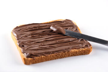 A slice of toast bread with chocolate hazelnut spread and a knife on a white background. Selective focus.