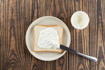 A slice of toast bread with cream cheese in a plate on a wooden table. Horizontal orientation, top view.