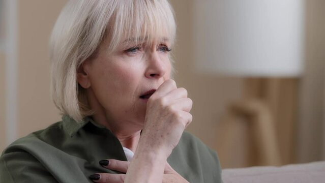 Portrait old woman coughing at home. Close up unwell Caucasian aging mature lady coughs having pain in chest coronavirus symptoms. Grandmother suffer from sore throat cold flu virus cough infection