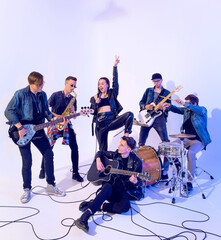 Fototapeta premium Young rock band of six people emotionally playing and singing on a white background with blue light around