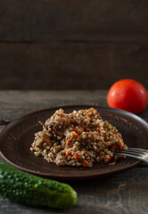 Dish plate of buckwheat porridge with carrots and meat. Fork, cucumber tomato