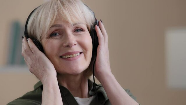 Beautiful old caucasian woman in headphones happy carefree grandmother relaxes to songs enjoys listening chill music listens musical composition in modern earphones and dances relaxing audio sound mp3