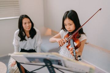 自宅でバイオリンの練習をする母と娘  © Adobe Stock
