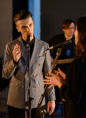 A young Caucasian vocalist sings against the background of a band and looks at the vocalist