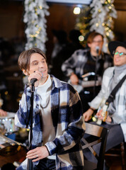 Young vocalist sings into a microphone on the background of a Christmas tree and a rock band