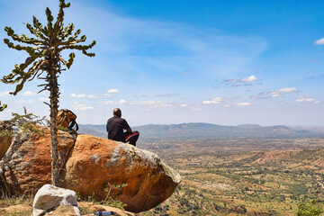 Rear view of a hiker sitting on a rock at a scenic view point in Makueni, Kenya