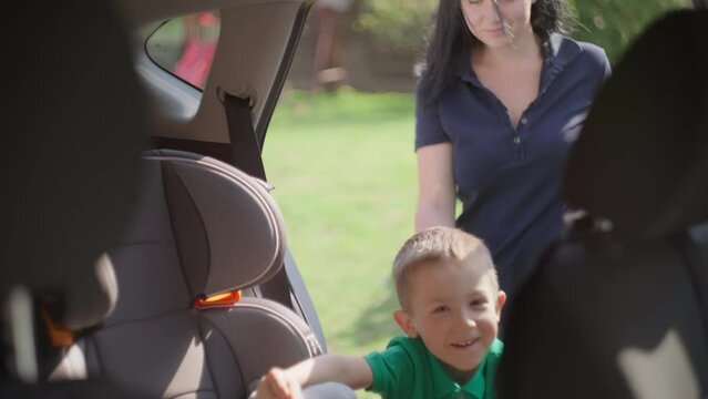 Mom and son go to the car, the child gets into a child car seat. Woman fastens a boy with a seat belt.