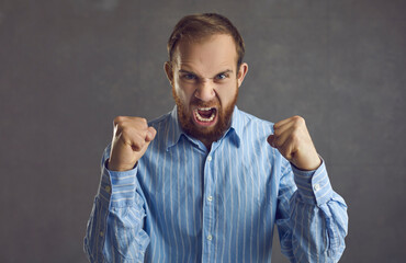 Studio shot of crazy angry aggressive young man clenching fists and screaming. Mad frustrated male...