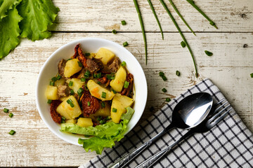 Stewed potatoes in a white cup on a white wooden table, cutlery and a checkered towel, food photo...