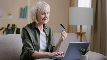 Fototapeta na wymiar Elderly Caucasian 60s woman internet shopping on laptop at home. Senior adult mature lady e-commerce buying paying in computer app virtual money with credit card online sitting on sofa in living room