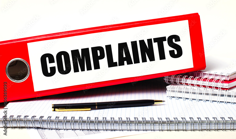 Poster on the desktop are notebooks, a pen and a red folder for papers with the text complaints. business c