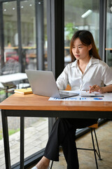 Female accountant focusing on her tasks, calculating and reviewing the report on laptop.