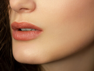 Close-up of woman's lips with fashion natural beige lipstick makeup. Macro sexy pale lipgloss make-up . Gentle pure skin and wavy brunet hair. Cosmetology, Spa, increase in lips