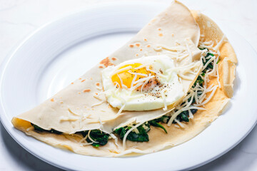 pancake stuffed with spinach leaves served with fried egg and grated cheese