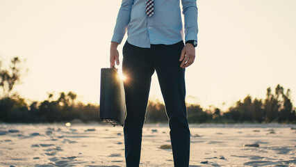 businessman on the beach with black briefcase at sunset.