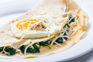 pancake stuffed with spinach leaves served with fried egg and grated cheese