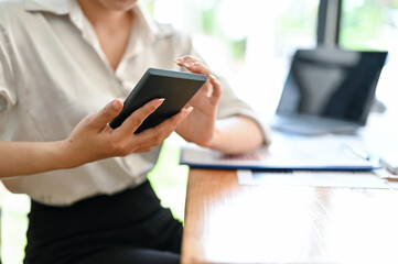 Female sitting at her office desk, using smartphone. cropped image