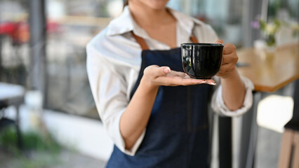 Cropped image, Female barista holding a black cup of coffee