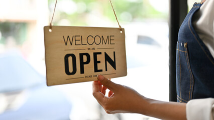 Female waitress or barista hanging a welcome sign in front of the restaurant door.