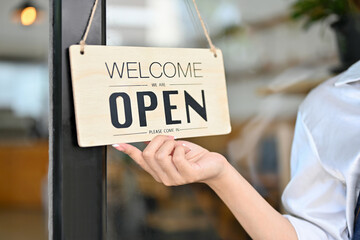 Female barista holding a coffee shop welcome sign in front of the coffee shop.