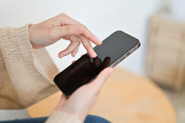 Female using a smartphone in her living room. Phone black screen mockup.