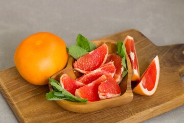 Juicy fresh grapefruit slices with fresh mint in a bowl on a wooden board