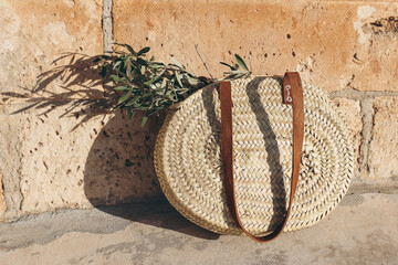 Summer vacation still life. Round French straw basket with leather handles and green olive tree...