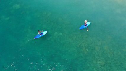 Aerial drone view of couple exercising sup board in turquoise tropical clear open sea