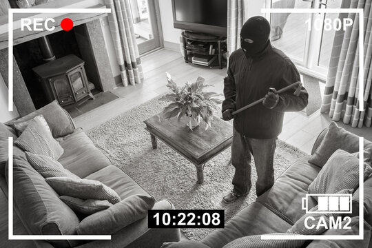 CCTV surveillance security camera of burglar breaking into home through back door window with crowbar