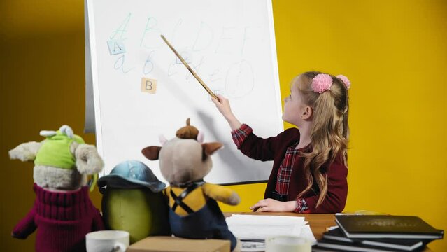 A little girl is playing teacher with her toys on a yellow background. Children as adults