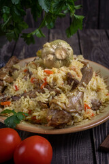Uzbek pilaf with duck and garlic in a plate on a dark background