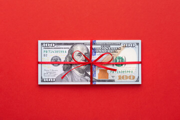 Dollar bills tied with a red ribbon on red background. Financial bonus, gift and charity concept.