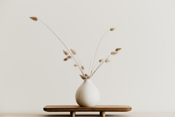 A bunch of  dried bunnytail flower in a white ceramic vase on a brown wooden board. Simple and...