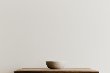A beige ceramic bowl on a brown wooden board in front of a white wall. Hand made bowl with copy space. Minimal concept, simple design. 