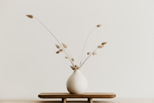 Fototapeta A bunch of  dried bunnytail flower in a white ceramic vase on a brown wooden board. Simple and minimal home decoration. White wall, copy space. 