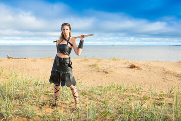 female warrior wearing dark leather armor with iron falchion in her hand is standing on the seaside