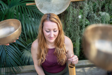Yoga concept, meditation and sound therapy. Beautiful young caucasian woman surrounded by copper...