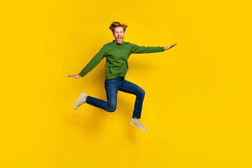 Fototapeta na wymiar Full length photo of excited impressed man wear green pullover jumping high isolated yellow color background