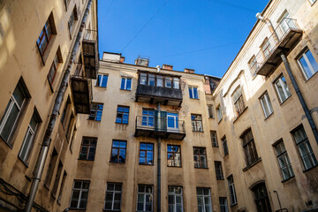 Fototapeta na wymiar Saint Petersburg, Russia, 17 October 2021: Hight narrow courtyards called well in center, old architecture, Bottom up view, piece of sky is visible between profitable yellow houses, Dark inner