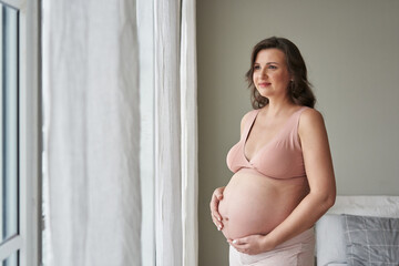 beautiful pregnant woman at the window in the bedroom. waiting for the baby. pregnant belly