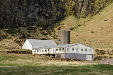 Fototapeta na wymiar Skogar, Iceland, April 22, 2022: modern agricaultural barns and silo against the backdrop of a rocky cliff